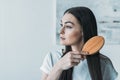 young brunette woman combing hair with hairbrush and looking away Royalty Free Stock Photo