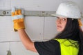 Young brunette woman construction worker in white hard hat and green high visibility vest, measuring wall with spirit bubble level Royalty Free Stock Photo
