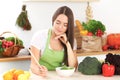 Young brunette woman is cooking or eating fresh salad in the kitchen. Housewife holding wooden spoon in her right hand Royalty Free Stock Photo