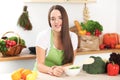 Young brunette woman is cooking or eating fresh salad in the kitchen. Housewife holding wooden spoon in her right hand Royalty Free Stock Photo