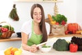 Young brunette woman is cooking or eating fresh salad in the kitchen. Housewife holding wooden spoon in her right hand Royalty Free Stock Photo