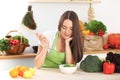 Young brunette woman is cooking or eating fresh salad in the kitchen. Housewife holding wooden spoon in her right hand Royalty Free Stock Photo