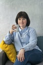 Young brunette woman with cup in sits on couch and looks at camera. Business woman resting during lunch break