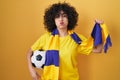 Young brunette woman with curly hair football hooligan holding ball puffing cheeks with funny face