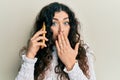 Young brunette woman with curly hair having conversation talking on the smartphone covering mouth with hand, shocked and afraid Royalty Free Stock Photo