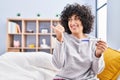 Young brunette woman with curly hair holding pregnancy test result pointing thumb up to the side smiling happy with open mouth Royalty Free Stock Photo