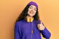 Young brunette woman with curly hair listening to music using headphones doing happy thumbs up gesture with hand Royalty Free Stock Photo