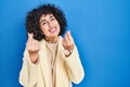 Young brunette woman with curly hair standing over blue background doing money gesture with hands, asking for salary payment, Royalty Free Stock Photo