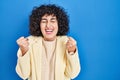Young brunette woman with curly hair standing over blue background excited for success with arms raised and eyes closed Royalty Free Stock Photo