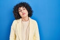 Young brunette woman with curly hair standing over blue background looking sleepy and tired, exhausted for fatigue and hangover, Royalty Free Stock Photo