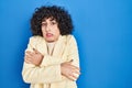 Young brunette woman with curly hair standing over blue background shaking and freezing for winter cold with sad and shock Royalty Free Stock Photo