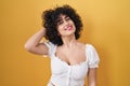 Young brunette woman with curly hair standing over yellow background smiling confident touching hair with hand up gesture, posing Royalty Free Stock Photo