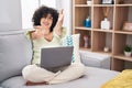 Young brunette woman with curly hair using laptop sitting on the sofa at home looking at the camera smiling with open arms for hug Royalty Free Stock Photo