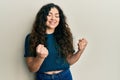 Young brunette woman with curly hair wearing casual clothes excited for success with arms raised and eyes closed celebrating Royalty Free Stock Photo