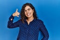 Young brunette woman with curly hair wearing casual clothes over blue background smiling doing phone gesture with hand and fingers Royalty Free Stock Photo