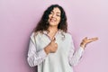 Young brunette woman with curly hair wearing casual clothes showing palm hand and doing ok gesture with thumbs up, smiling happy Royalty Free Stock Photo