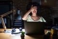 Young brunette woman with curly hair working at the office at night smiling and laughing with hand on face covering eyes for Royalty Free Stock Photo