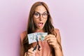 Young brunette woman cutting dollars with scissors for currency devaluation afraid and shocked with surprise and amazed Royalty Free Stock Photo