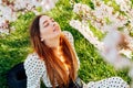 Young brunette woman in dress with closed eyes sitting near a pink blooming tree and enjoying the sunshine. Generation Z Royalty Free Stock Photo