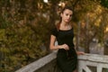Young brunette woman dressed in black slim dress, hair arranged in ponytail posing on the balcony, looking at camera. Royalty Free Stock Photo