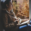 Young brunette woman drinking a cup of tea or coffee and reading a book. Female sitting at home by the window and read a book Royalty Free Stock Photo