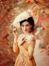 A young brunette woman with an elegant, hairstyle in a hat with a strass feathers. Lady in a yellow vintage dress walks through th Royalty Free Stock Photo