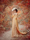 A young brunette woman with an elegant, hairstyle in a hat with a strass feathers. Lady in a yellow vintage dress walks