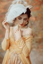 A young brunette woman with an elegant, hairstyle in a hat with a strass feathers. Lady in a yellow vintage dress walks Royalty Free Stock Photo