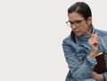 A young brunette woman in glasses and a denim jacket sits with a pensive look with a pen and notepad in her hands. Free space for Royalty Free Stock Photo