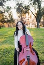 Happy young brunette woman with glasses smiling and playing cello at sunset in the park. Vertical. Copy space Royalty Free Stock Photo