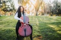 Young brunette woman with glasses playing cello at sunset in the park, on a green grass. Copy space. Royalty Free Stock Photo