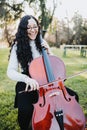 Young brunette woman with glasses playing cello at sunset in the park, on a green grass. Vertical Royalty Free Stock Photo