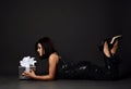 Young brunette woman in glittering black cocktail dress is lying on floor holding looking at holiday present box Royalty Free Stock Photo