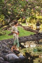 Young brunette woman in green dress walking in japanese garden stone waterfront