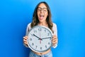 Young brunette woman holding big clock smiling and laughing hard out loud because funny crazy joke Royalty Free Stock Photo
