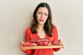 Young brunette woman holding board with raw meat in shock face, looking skeptical and sarcastic, surprised with open mouth Royalty Free Stock Photo