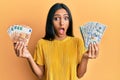 Young brunette woman holding bunch of dollars and euros afraid and shocked with surprise and amazed expression, fear and excited Royalty Free Stock Photo