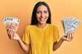 Young brunette woman holding bunch of dollars and euros smiling and laughing hard out loud because funny crazy joke Royalty Free Stock Photo