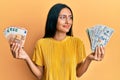 Young brunette woman holding bunch of dollars and euros smiling looking to the side and staring away thinking Royalty Free Stock Photo