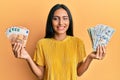 Young brunette woman holding bunch of dollars and euros winking looking at the camera with sexy expression, cheerful and happy Royalty Free Stock Photo