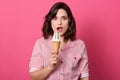 Young brunette woman holding cornet ice cream isolated over pink background, girl looks surprised and keeping mouth widely opened Royalty Free Stock Photo