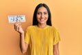 Young brunette woman holding 100 dollars banknote looking positive and happy standing and smiling with a confident smile showing Royalty Free Stock Photo