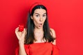 Young brunette woman holding engagement ring for proposal scared and amazed with open mouth for surprise, disbelief face Royalty Free Stock Photo