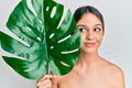 Young brunette woman holding green plant leaf close to beautiful face smiling looking to the side and staring away thinking Royalty Free Stock Photo