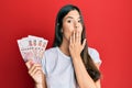 Young brunette woman holding hong kong 100 dollars banknotes covering mouth with hand, shocked and afraid for mistake Royalty Free Stock Photo