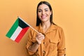 Young brunette woman holding kuwait flag looking positive and happy standing and smiling with a confident smile showing teeth