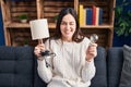 Young brunette woman holding led lightbulb and lamp winking looking at the camera with sexy expression, cheerful and happy face Royalty Free Stock Photo