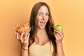 Young brunette woman holding nachos and healthy green apple winking looking at the camera with sexy expression, cheerful and happy Royalty Free Stock Photo