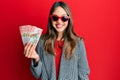 Young brunette woman holding 100 new zealand dollars banknote looking positive and happy standing and smiling with a confident Royalty Free Stock Photo