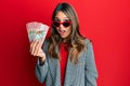 Young brunette woman holding 100 new zealand dollars banknote scared and amazed with open mouth for surprise, disbelief face Royalty Free Stock Photo